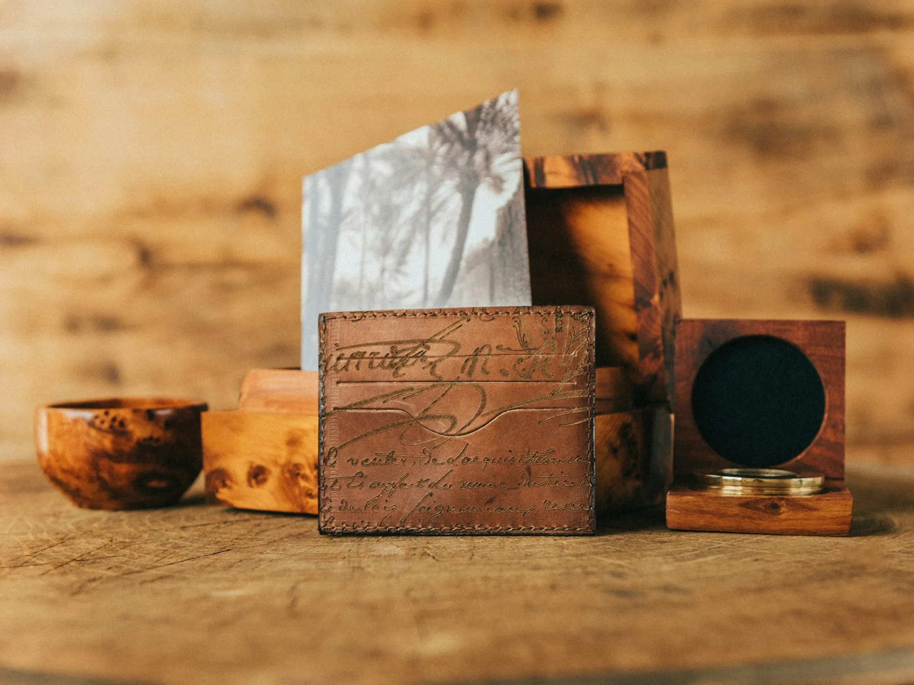 A leather wallet engraved with handwritten script, resting against burl wood boxes on a workbench