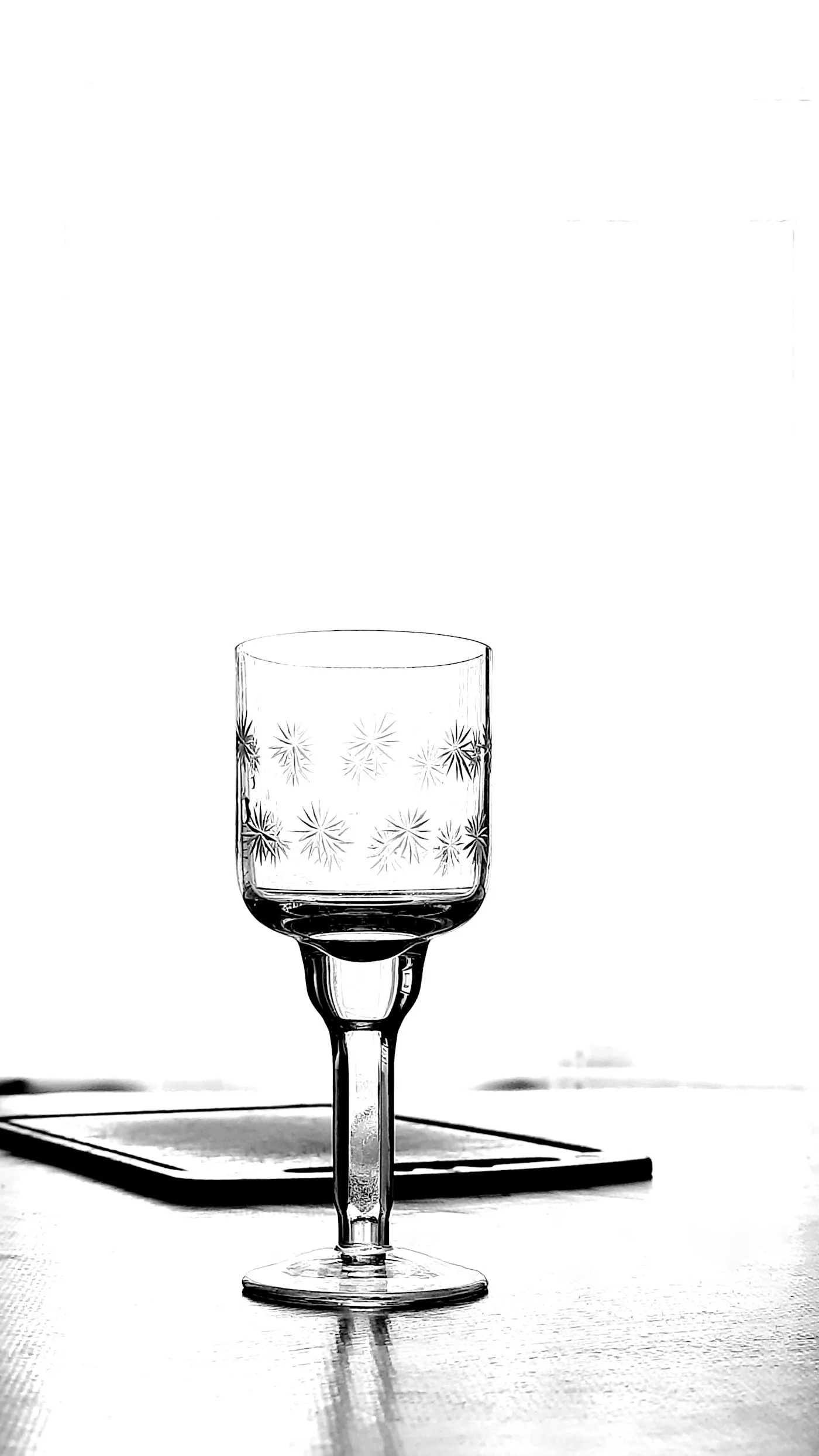 A single stemmed glass etched with a pattern of starbursts, lit from behind against a bright white background